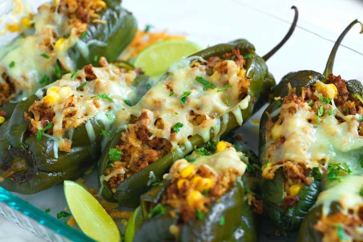 Whole poblano peppers, shredded cheese, onion, garlic, and canned tomatoes arranged on a clean kitchen counter with warm natural light