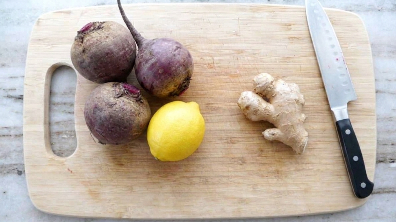 Whole raw beets, a lemon, and a knob of ginger arranged on a cutting board