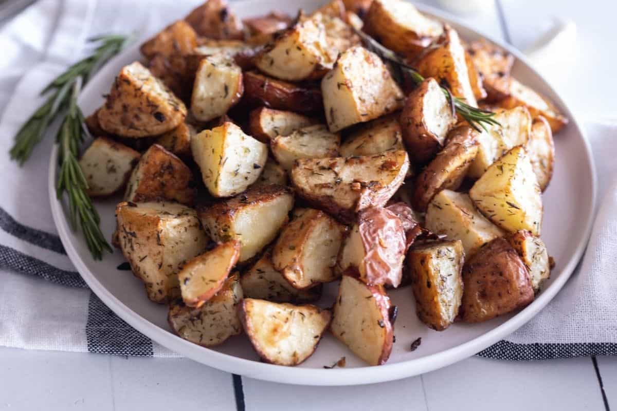 Whole red potatoes, a small bowl of olive oil, garlic cloves, kosher salt, black pepper, paprika, and dried herbs arranged on a simple kitchen counter