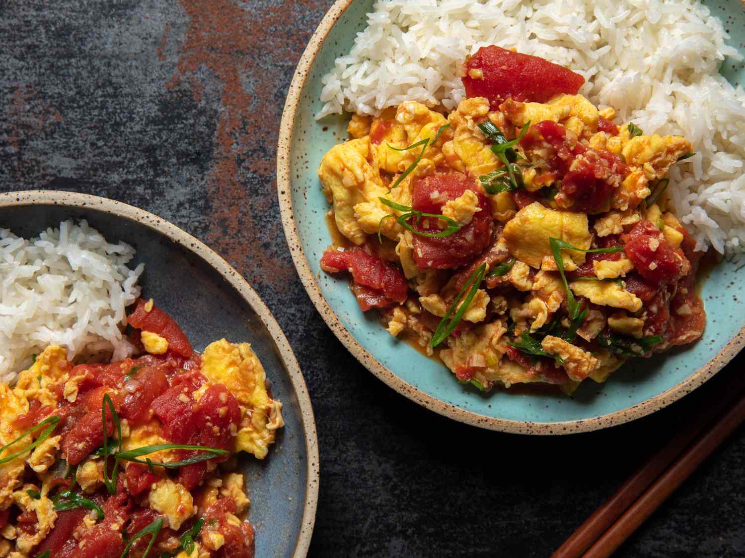 Whole tomatoes, eggs, scallions, garlic, and small bowls of soy sauce, sugar, and cornstarch arranged on a clean kitchen counter under warm light