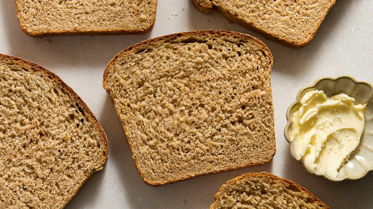 Whole wheat flour, instant yeast, salt, honey, olive oil, and a small bowl of vital wheat gluten arranged on a clean kitchen counter
