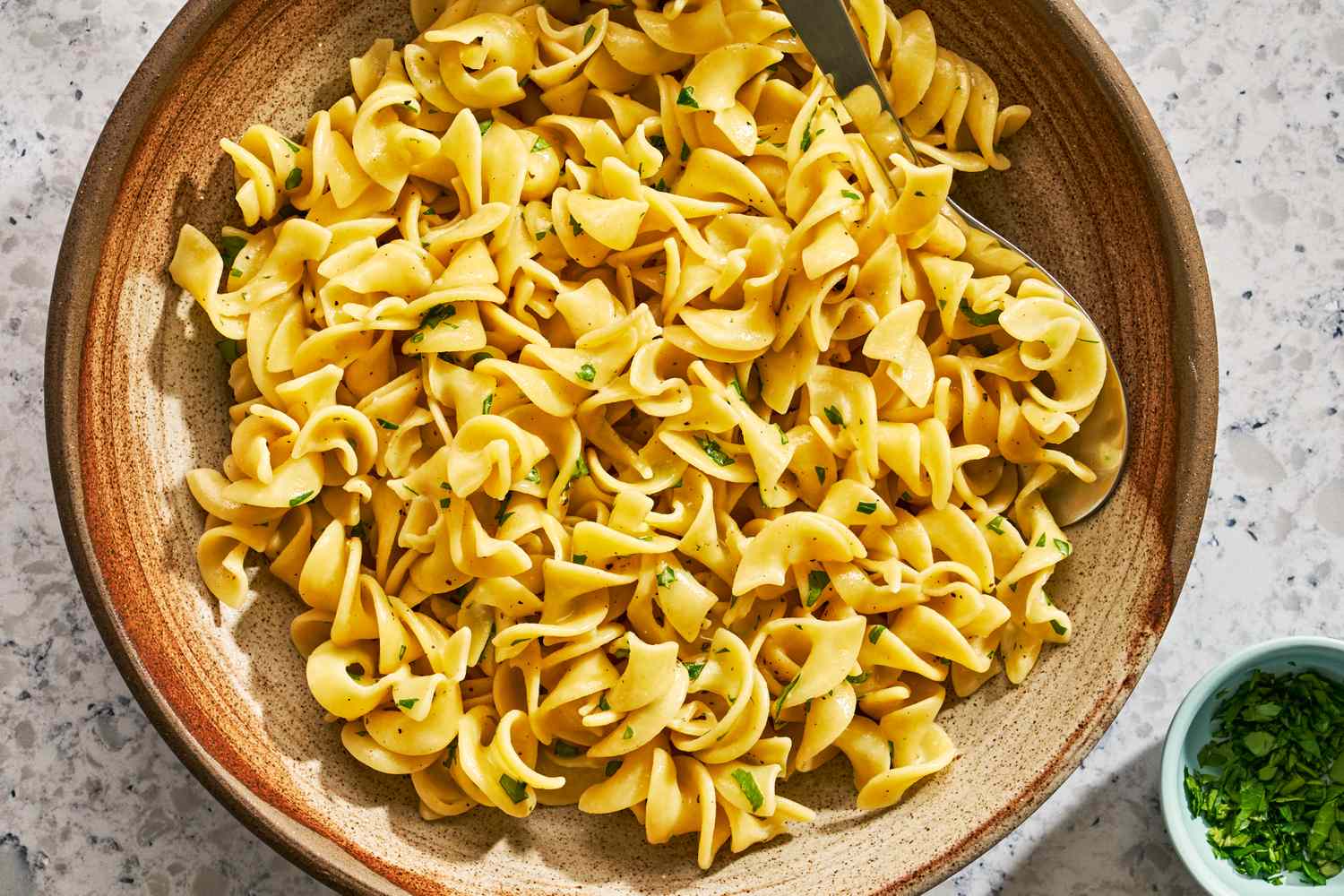 Wide egg noodles drained in a colander over a sink with steam rising, in a bright home kitchen