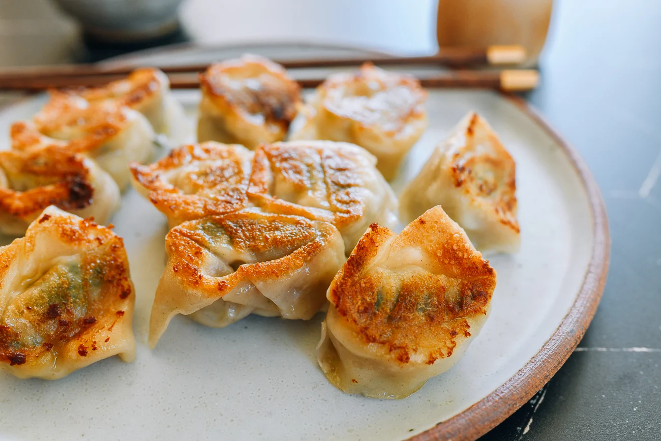 Wontons sizzling in a nonstick skillet with browned bottoms while tongs hover nearby, ready to transfer them to a plate