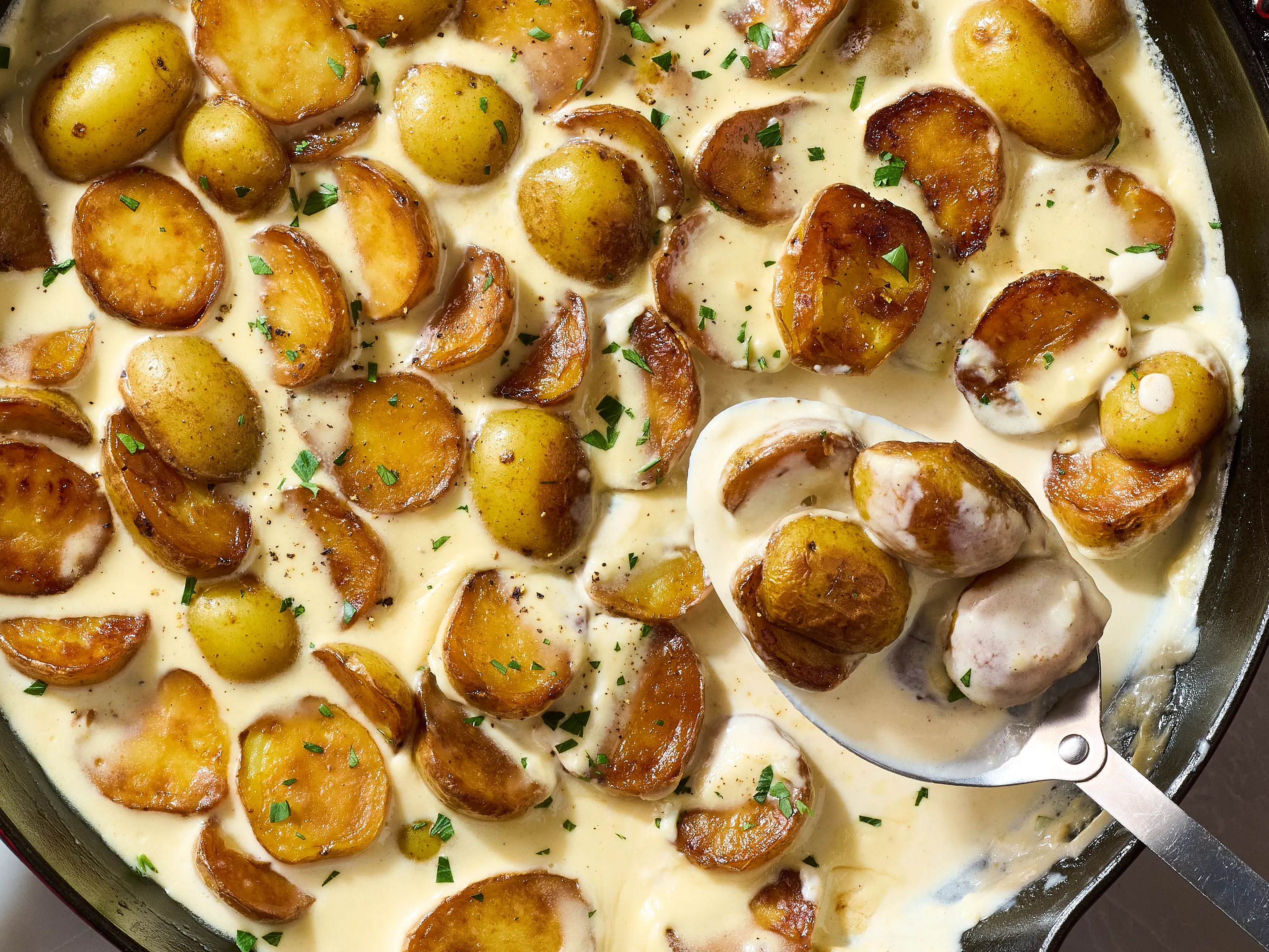 Yukon Gold potatoes, garlic cloves, and a measuring cup of cream on a kitchen counter