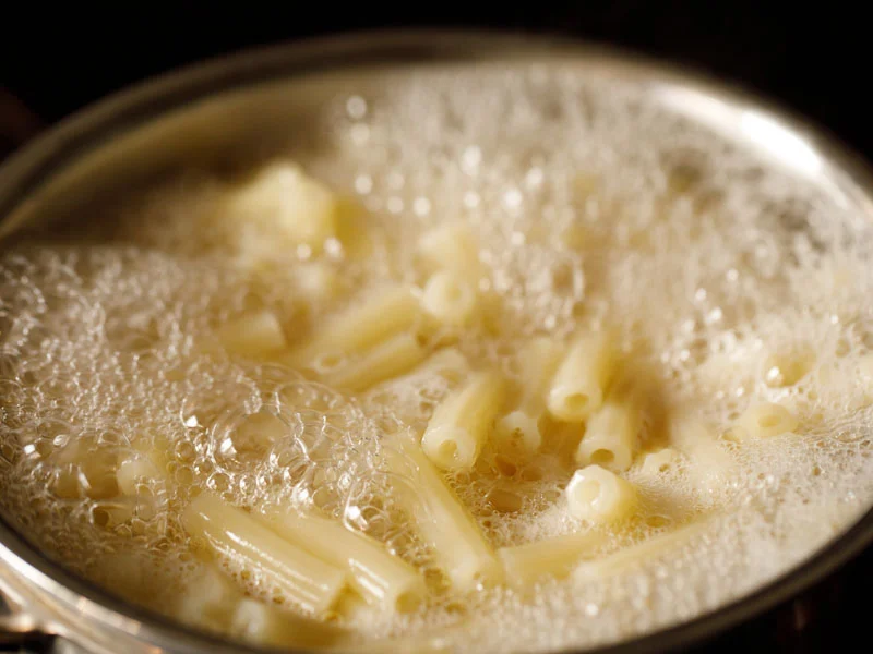 Ziti pasta boiling in a large stainless steel pot on a home stove with steam rising
