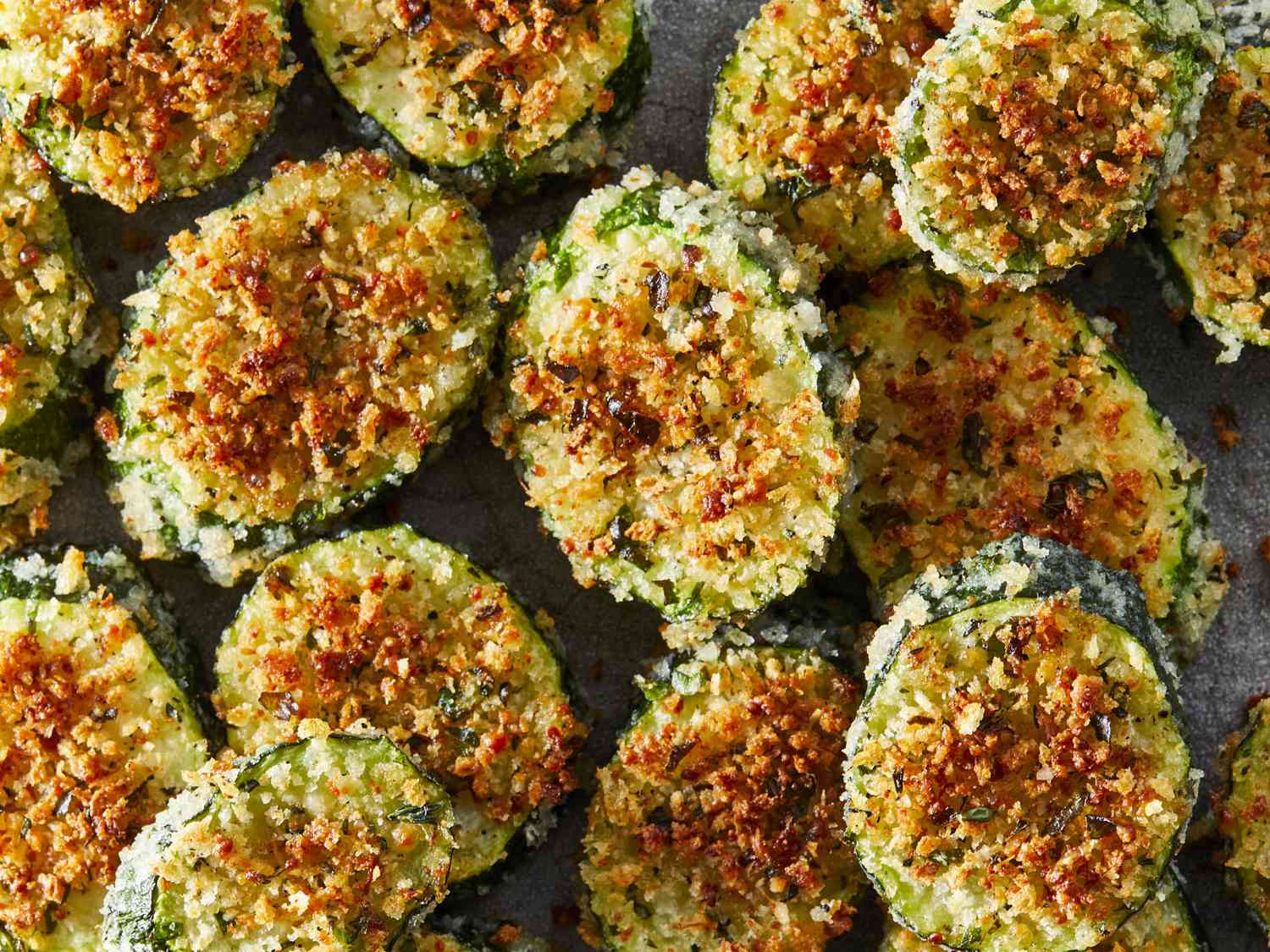 Zucchini, eggs, grated Parmesan, breadcrumbs, garlic powder, and spices arranged on a light kitchen counter with measuring spoons