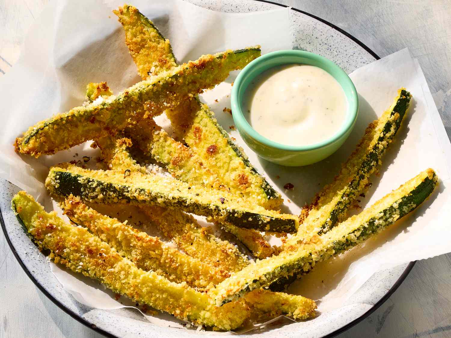 Zucchini, panko breadcrumbs, parmesan, eggs, garlic powder, paprika, salt, pepper, and olive oil arranged on a clean kitchen counter