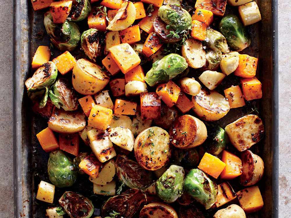 Zucchini, peppers, red onion, and mushrooms roasting on a sheet pan with browned edges in a home oven, warm kitchen lighting